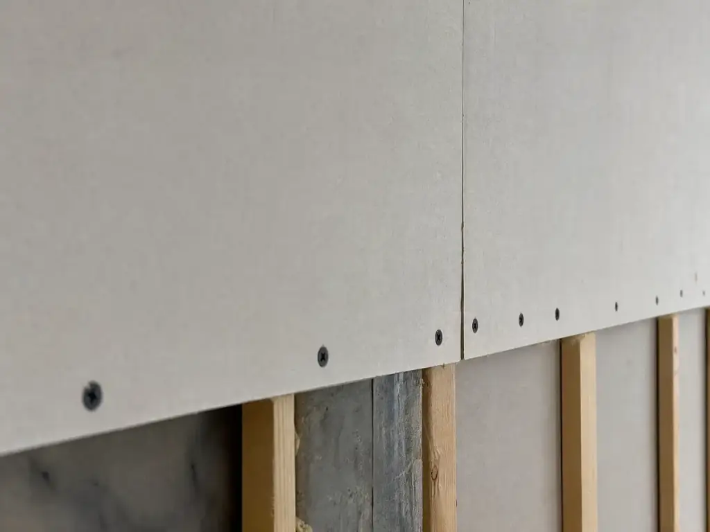 Row of drywall screws set just below the paper face along a stud