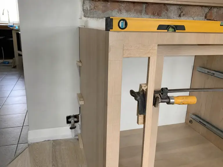 Cabinet being shimmed and levelled against a wall with a clamp joining two stiles