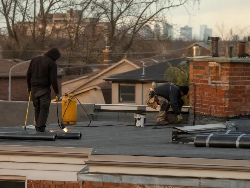 Roofers working on a low slope flat roof with rolls of membrane and a parapet wall