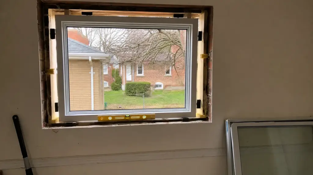 New window unit being set into a brick opening with shims and a level in the reveal