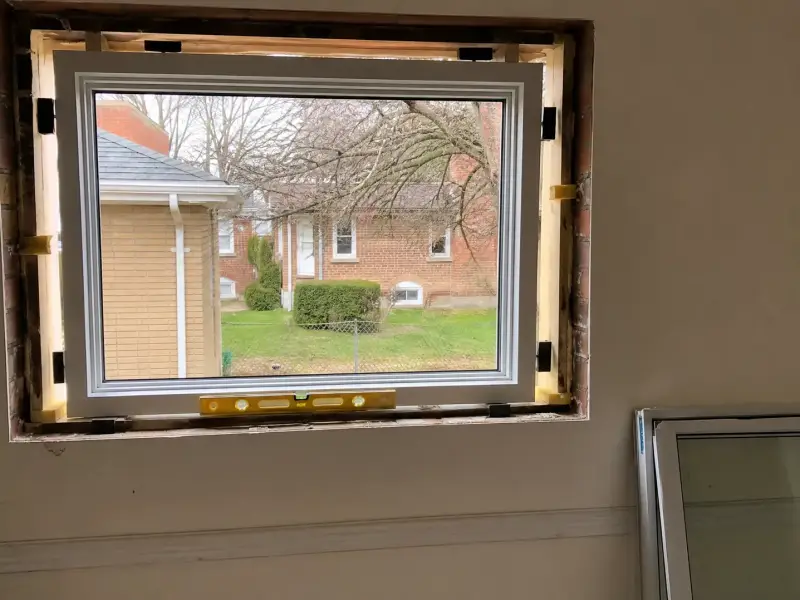 New window unit being set into a brick opening with shims and a level in the reveal